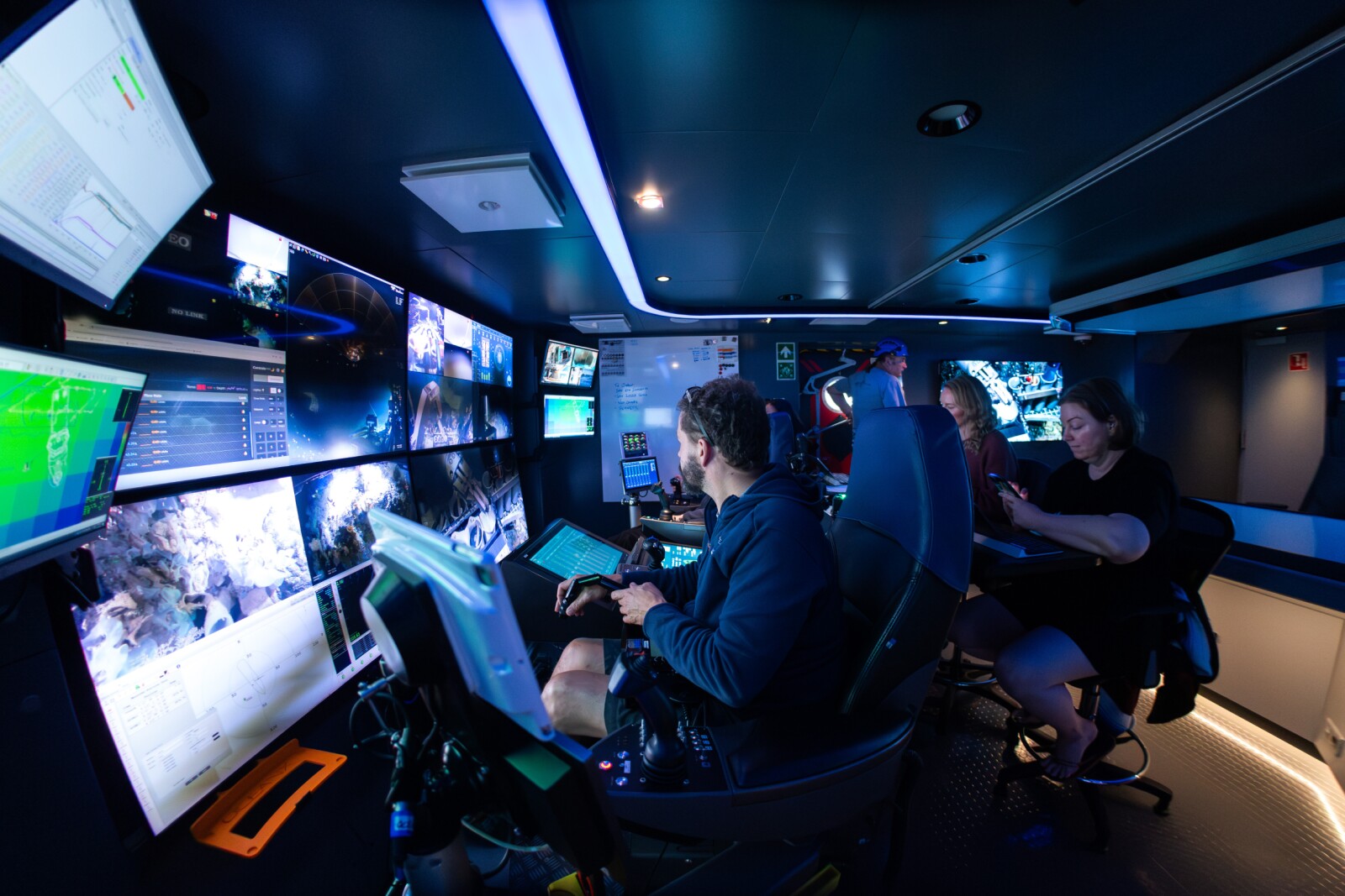 Scientists monitor a deep-sea sampling dive from Mission Control aboard OceanXplorer as an ROV pilot navigates ROV Chimaera.